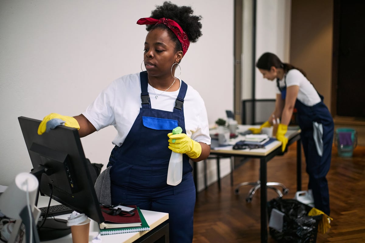 Professional cleaning team sanitizing a modern office computer workstation
